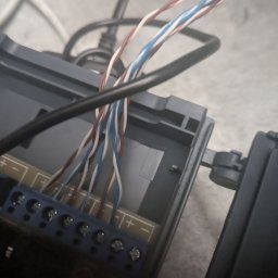 Dominik Borowski - Podłączenie przewodów (białe, niebieskie, brązowe) do listwy zaciskowej wewnątrz obudowy urządzenia. Widoczne śruby mocujące przewody.