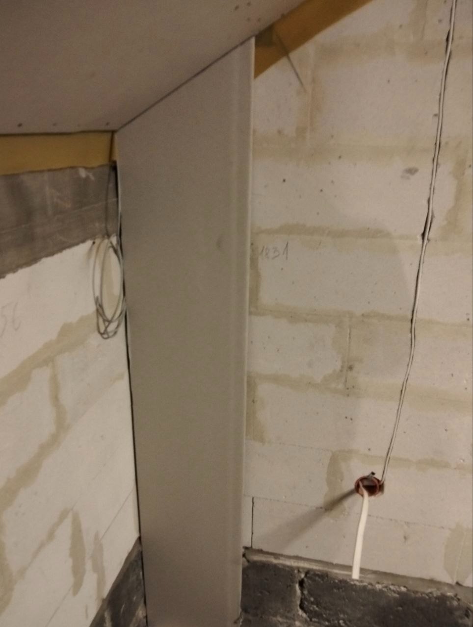 Narożnik ściany z instalacją elektryczną w trakcie prac wykończeniowych. Widoczne przewody i puszka elektryczna na tle surowej ściany z bloczków.