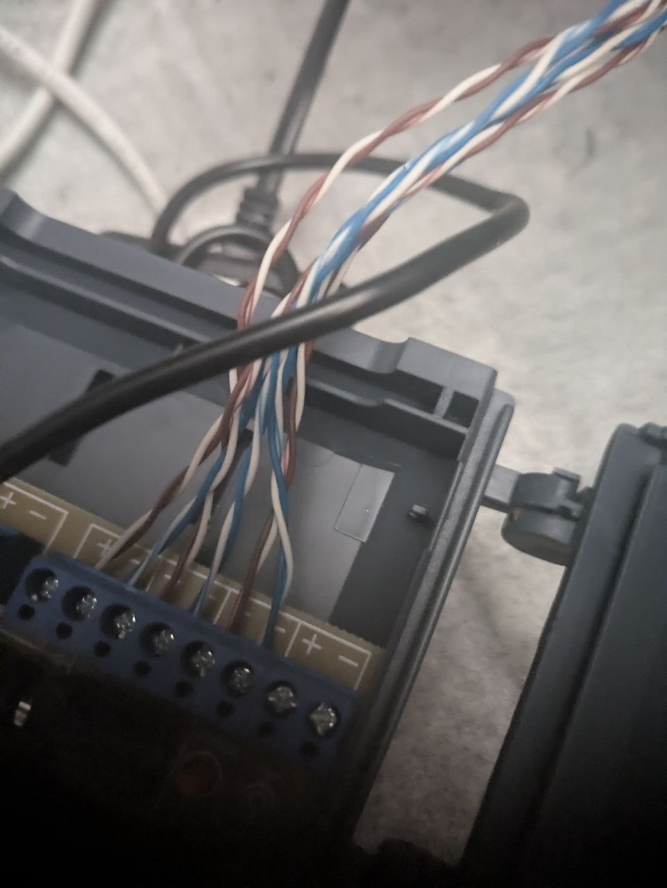 Podłączenie przewodów (białe, niebieskie, brązowe) do listwy zaciskowej wewnątrz obudowy urządzenia. Widoczne śruby mocujące przewody.