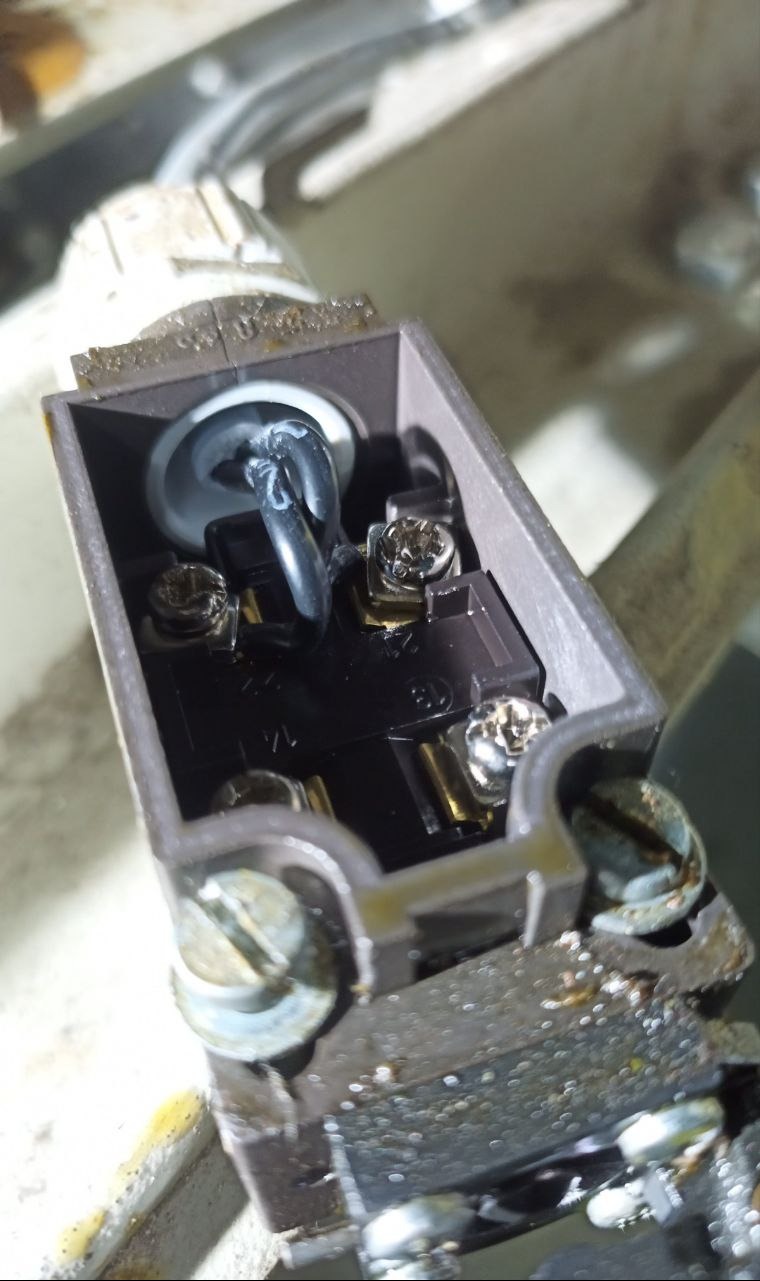 Zbliżenie na otwartą puszkę elektryczną z widocznymi przewodami i śrubami mocującymi, ukazującą detale połączeń elektrycznych wewnątrz.