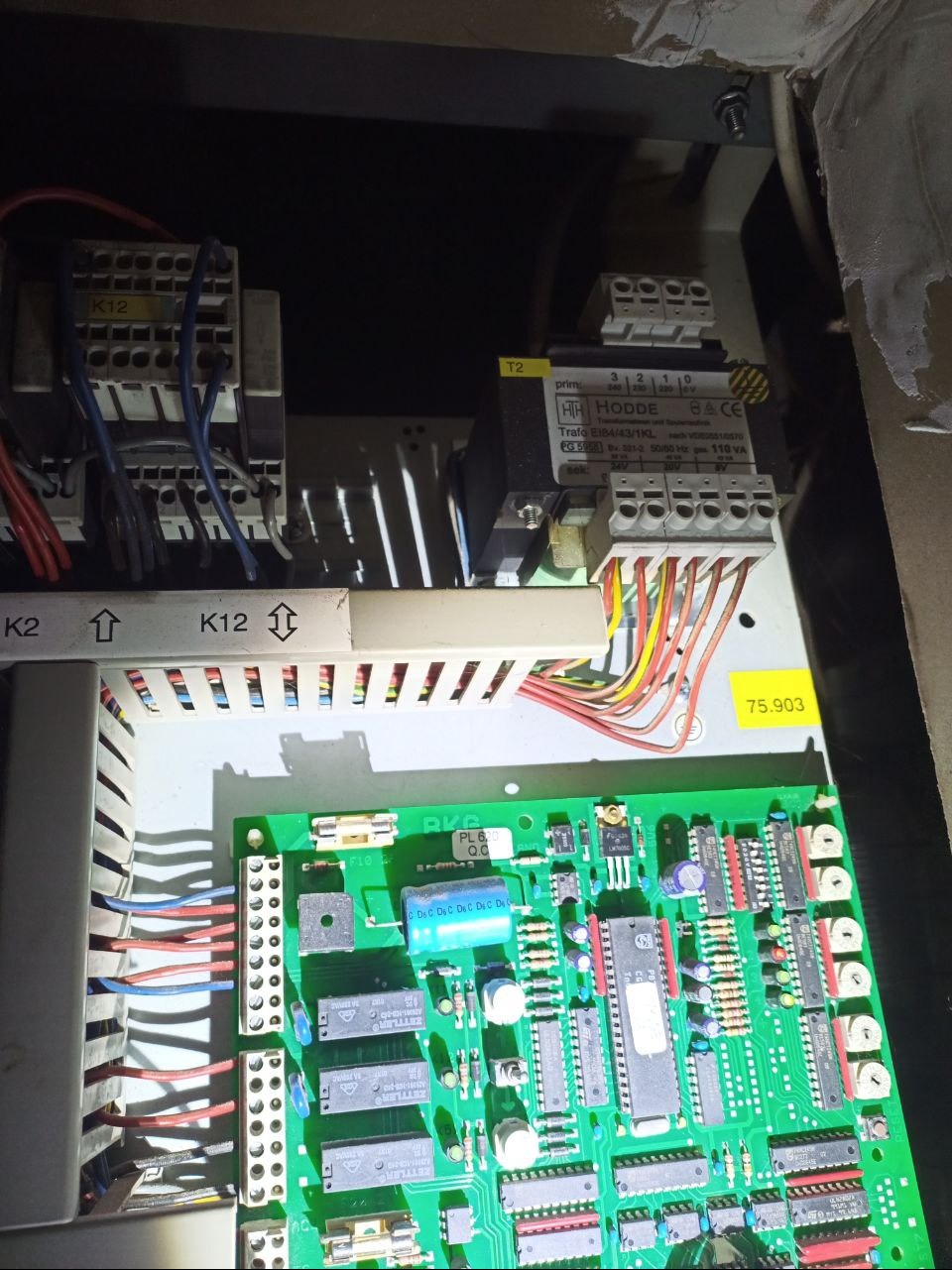 Otwarta skrzynka elektryczna z widoczną zieloną płytką drukowaną, transformatorem HODDE i licznymi przewodami. Widoczne oznaczenia K2 i K12.