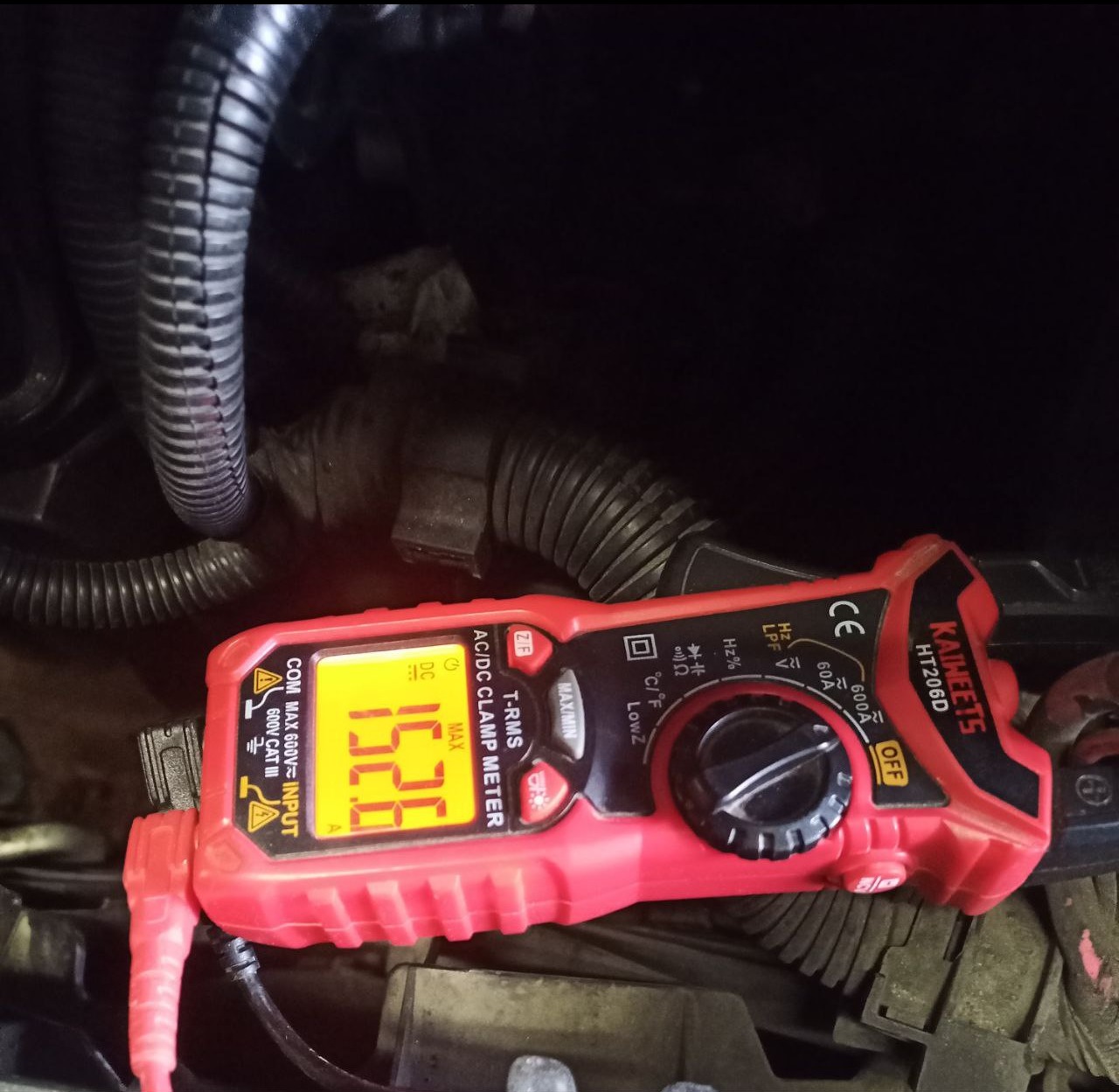 Czerwony miernik cęgowy Kaiweets HT206D z wyświetlaczem 152.6A, używany w trudno dostępnym miejscu, prawdopodobnie w komorze silnika pojazdu.