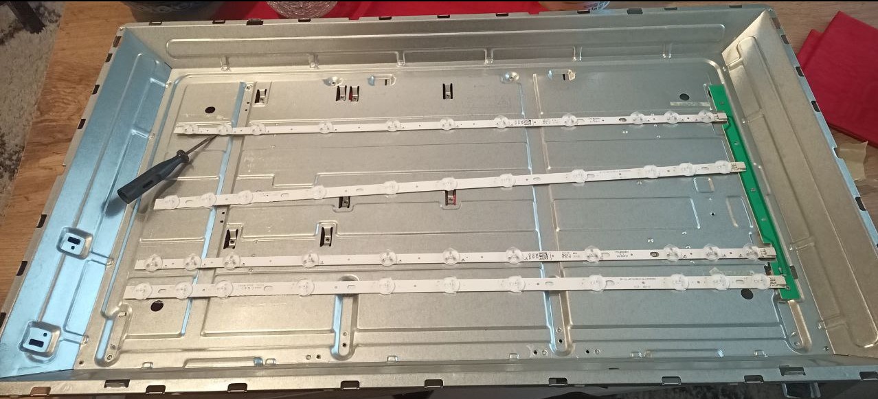 Wnętrze obudowy telewizora z zamontowanymi listwami LED. Widoczny śrubokręt, sugerujący naprawę lub wymianę podświetlenia. Metalowa konstrukcja i elementy elektroniczne.