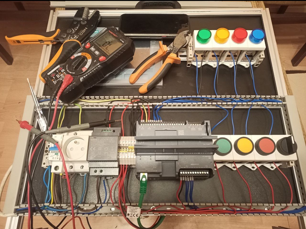 Panel sterowania z przyciskami, przewodami i miernikiem, w trakcie montażu. Widoczne narzędzia: obcinaczki, miernik uniwersalny. Elementy automatyki przemysłowej.