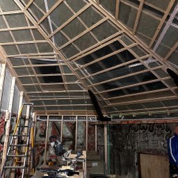 AK INVEST-BUD - Skośny sufit z drewnianą konstrukcją i izolacją z wełny mineralnej, widoczne narzędzia i drabina, ściany z graffiti. Prace wykończeniowe w surowym wnętrzu.