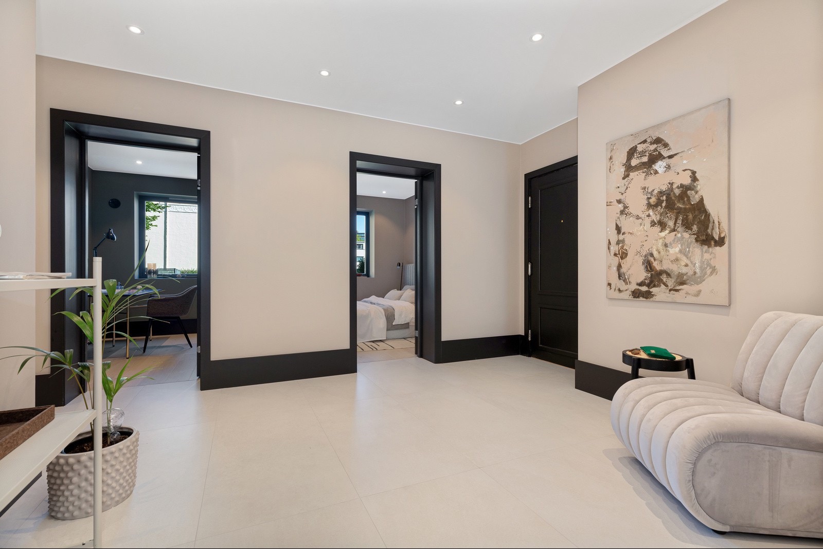 Jasne wnętrze z trzema parami drzwi z czarnymi futrynami, kremową sofą i abstrakcyjnym obrazem. Widok na pokój z biurkiem i sypialnię. Minimalistyczny design.