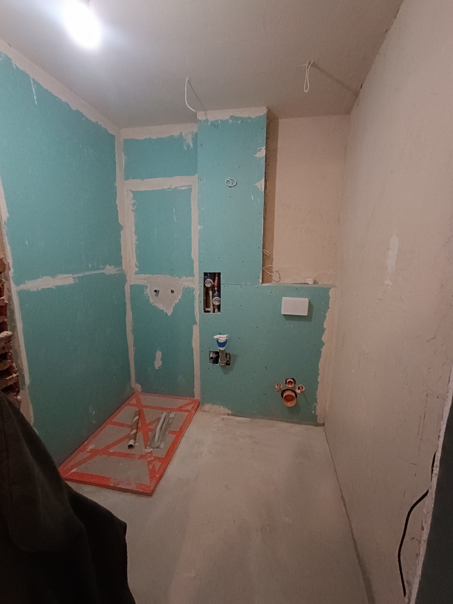 Łazienka w trakcie remontu: ściany z płyt karton-gips, widoczne instalacje hydrauliczne, przygotowany odpływ liniowy. Fragment ściany bez wykończenia.