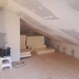 Remonovo - Poddasze w trakcie adaptacji: ocieplone skosy, płyty gipsowe na suficie, materiały izolacyjne składowane w pomieszczeniu, widoczny fragment drewnianej konstrukcji.