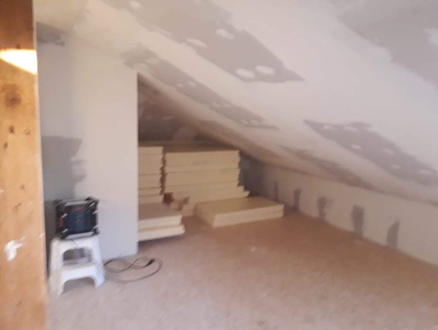 Poddasze w trakcie adaptacji: ocieplone skosy, płyty gipsowe na suficie, materiały izolacyjne składowane w pomieszczeniu, widoczny fragment drewnianej konstrukcji.