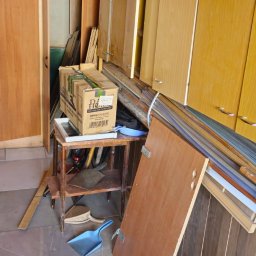 D.B Dariusz Błaszczyk - Pokój przed opróżnianiem: karton, meble do demontażu, szufelka. Widoczne ślady użytkowania i przygotowania do wywozu. Ujęcie z bliska, podkreślające stan pomieszczenia.