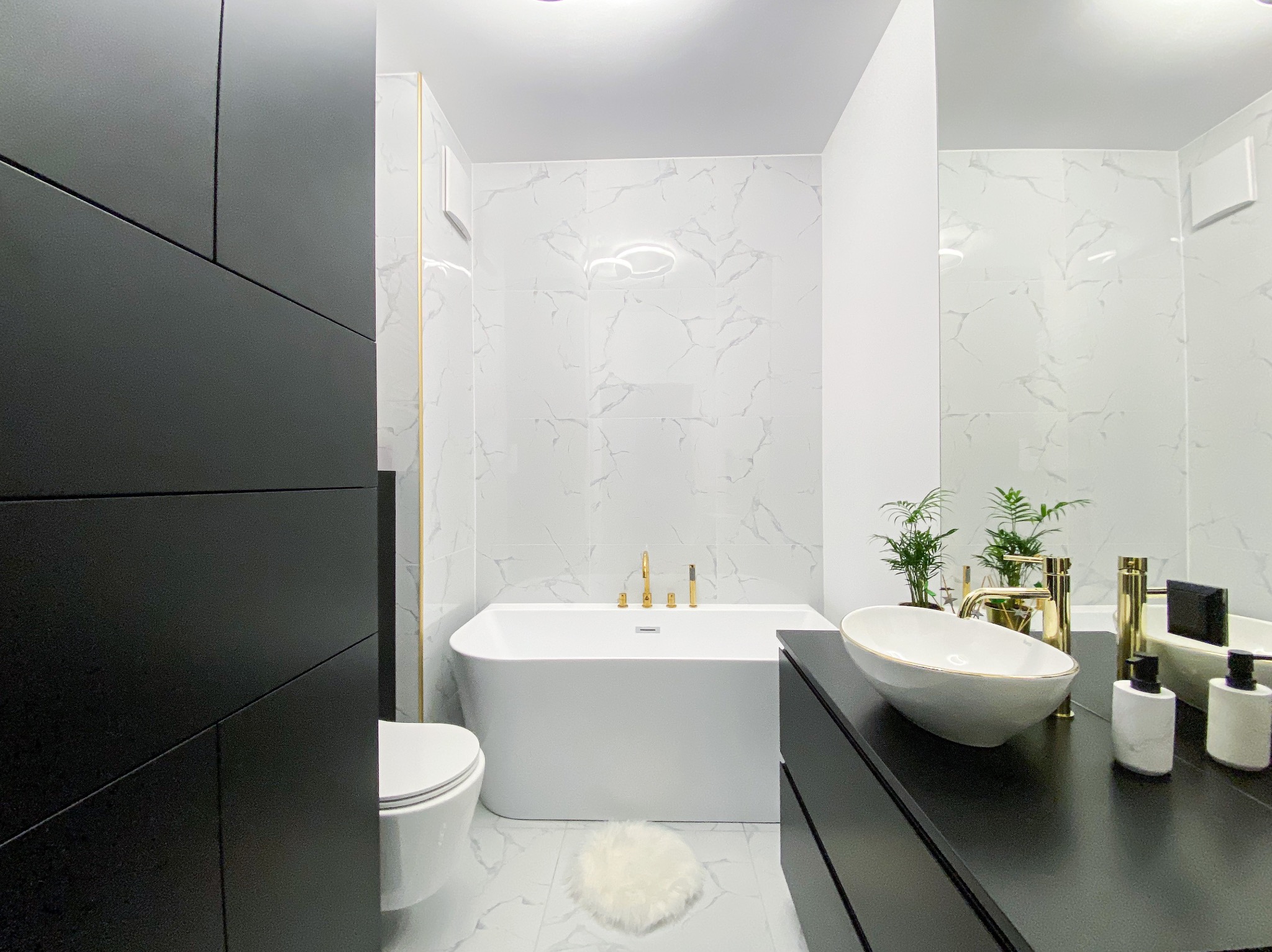 Nowoczesna łazienka z wanną, umywalką nablatową i czarnymi elementami. Marmurowe płytki na ścianach i podłodze. Złote akcenty armatury. Minimalistyczny design.