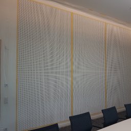 Malarz-Majster Artur Piejek - Biała ściana z perforacją zabezpieczona folią i taśmą malarską przed malowaniem w biurze. Widoczne krzesła i stół konferencyjny.