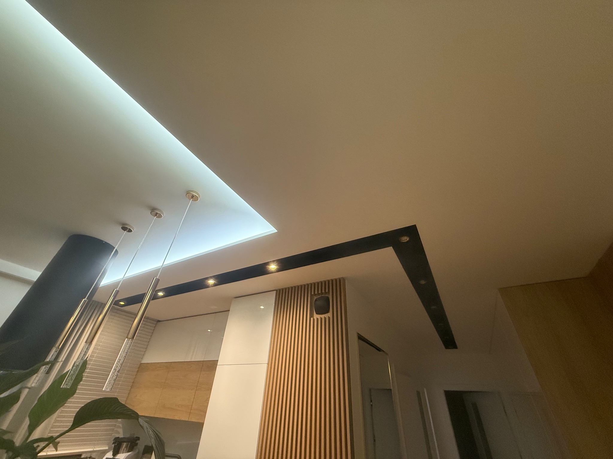 Nowoczesny sufit podwieszany z oświetleniem LED i dekoracyjnymi elementami wykończeniowymi. Widok z dołu, podkreślający geometrię i detale.