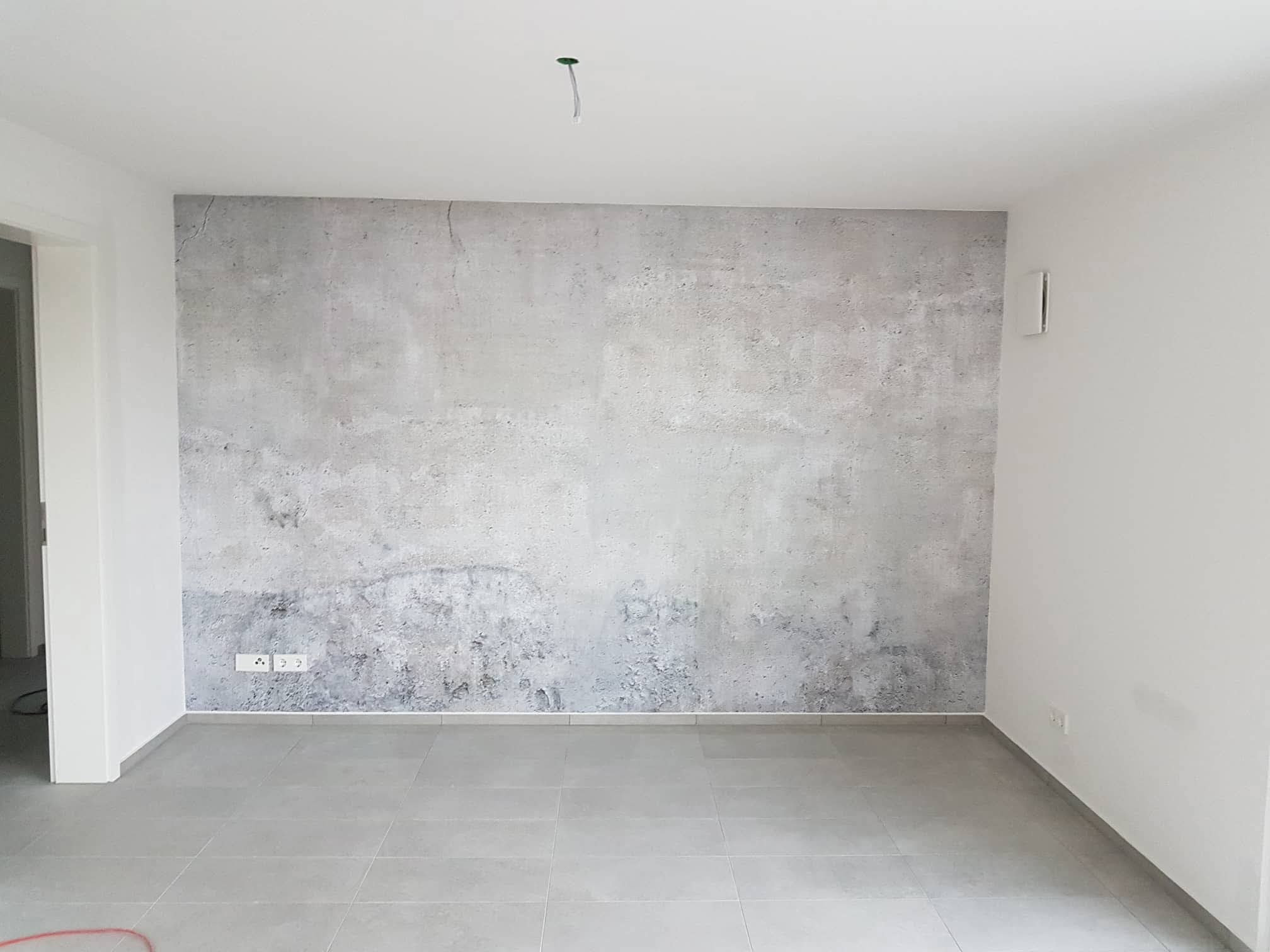 Szara ściana z efektem betonu w pustym pokoju z szarą podłogą z płytek. Widoczne gniazdka elektryczne i wystający kabel z sufitu. Minimalistyczne wykończenie wnętrza.