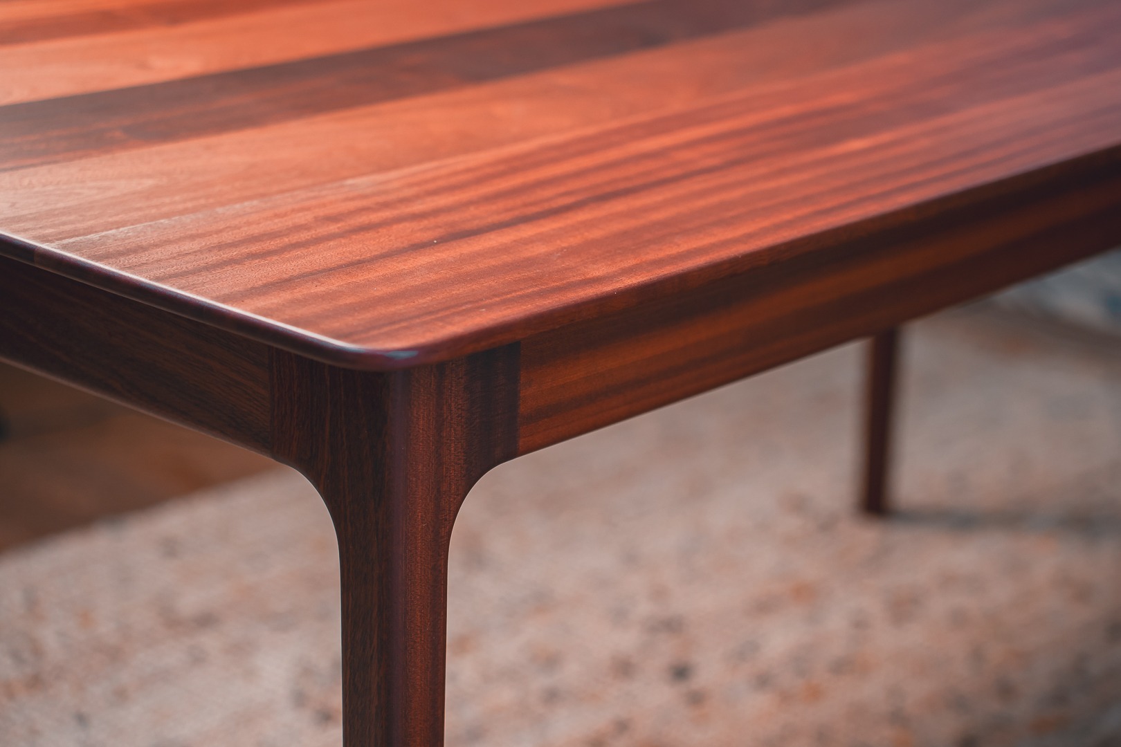 Detale wykończenia drewnianego stołu z blatem o bogatym usłojeniu i zaokrąglonych krawędziach, ukazujące precyzję wykonania i estetykę.