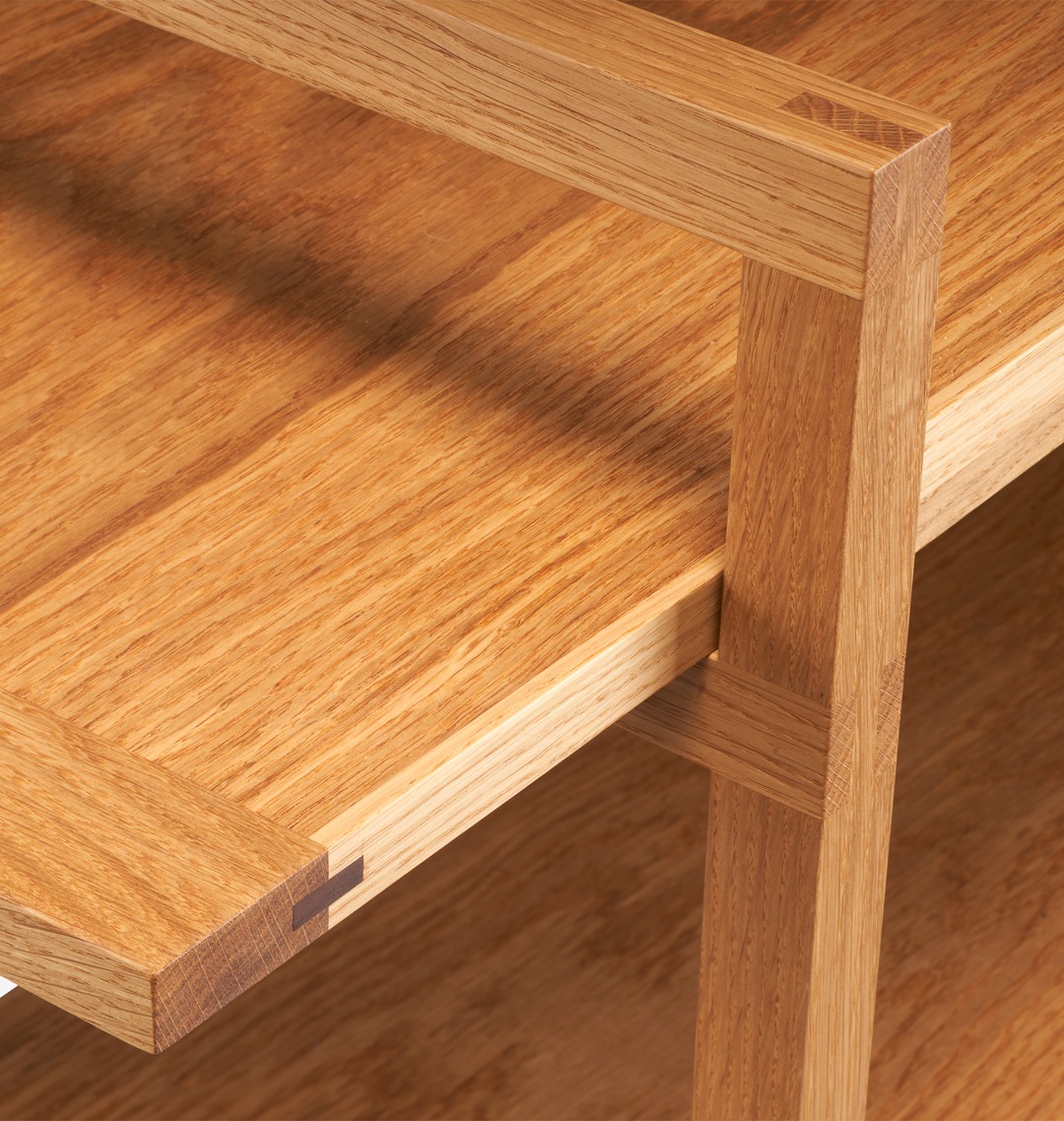 Detale konstrukcyjne dębowego regału: precyzyjne połączenia stolarskie, widoczna struktura drewna, ciepłe oświetlenie podkreśla naturalny odcień. Minimalistyczny design.