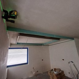 HQ Bartosz Pilarczyk - Sufit podwieszany z profili w trakcie montażu, poziomowany laserowo w Ozorkowie. Widoczne profile, okno i drabina. Ściany przygotowane pod gładzie.