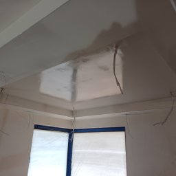 HQ Bartosz Pilarczyk - Świeżo pomalowany sufit z wystającymi przewodami elektrycznymi, okno zabezpieczone folią malarską. Widoczne ślady po szpachlowaniu.