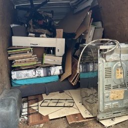 KM KRAS - Wnętrze brudnego busa wypełnionego meblami, kartonami i sprzętem AGD, przygotowanego do transportu. Widoczny fragment kuchenki i biurowe krzesło.