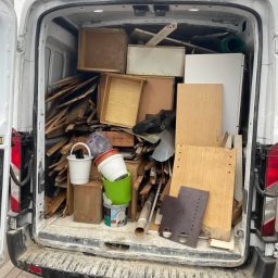 KM KRAS - Wnętrze brudnego busa wypełnione gruzem, drewnem i odpadami po remoncie. Widoczne otwarte tylne drzwi i fragment chodnika.