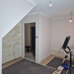 Heider-Remonty - Wnętrze w trakcie malowania: zabezpieczona podłoga, ściany częściowo pomalowane na jasny odcień, widoczny sprzęt malarski i oświetlenie robocze.