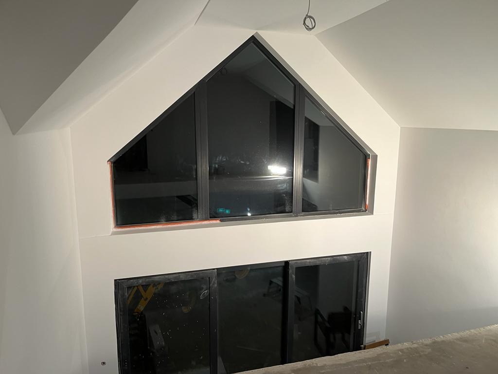 Wnętrze po malowaniu: białe ściany z oknami o nietypowych kształtach, widoczne ślady taśmy malarskiej, surowe wykończenie podłogi. Minimalistyczny design.