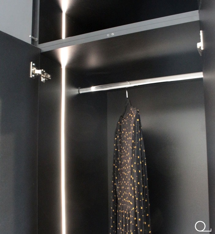 Wnętrze czarnej szafy wnękowej z oświetleniem LED, widoczna wisząca sukienka. Minimalistyczny design, nowoczesne wykończenie, metalowy drążek na ubrania.