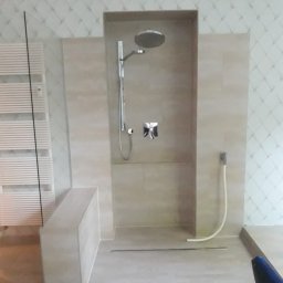 Aqua remont &secobau - Nowoczesna kabina prysznicowa typu walk-in z deszczownicą i odpływem liniowym, wykończona beżowymi płytkami, na tle ściany w romby. Minimalistyczny design.