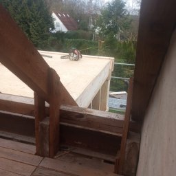Aqua remont &secobau - Konstrukcja drewniana dachu w trakcie budowy, widoczna piła łańcuchowa na płycie OSB, elementy więźby i fragment otoczenia z zielenią.
