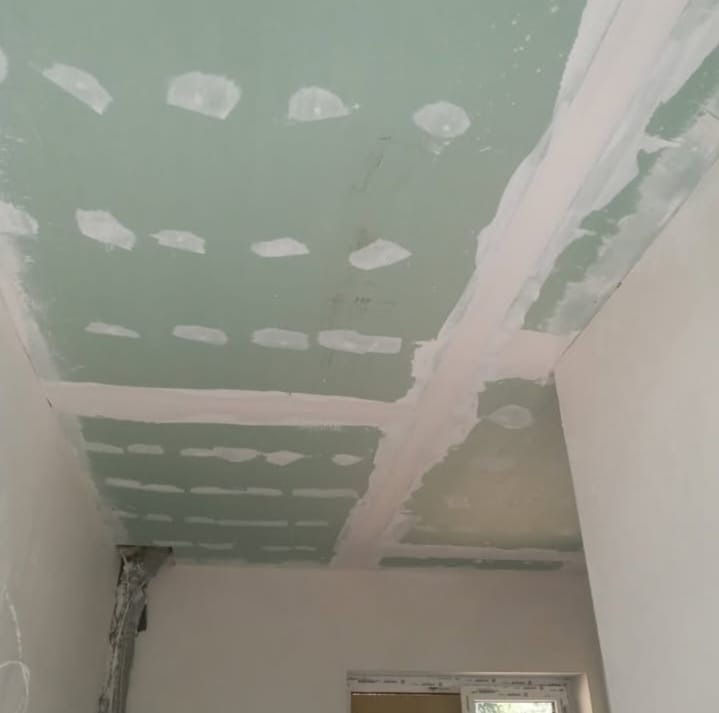 Zielony sufit z płyt gipsowo-kartonowych, z widocznymi łączeniami i miejscami po wkrętach, przygotowany do szpachlowania. Widok z dołu, fragment okna w tle.