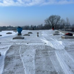 MMHigh - Odśnieżony dach płaski z widocznymi śladami odśnieżania, w tle zabudowa miejska i drzewa. Widoczne świetliki dachowe i elementy instalacji.