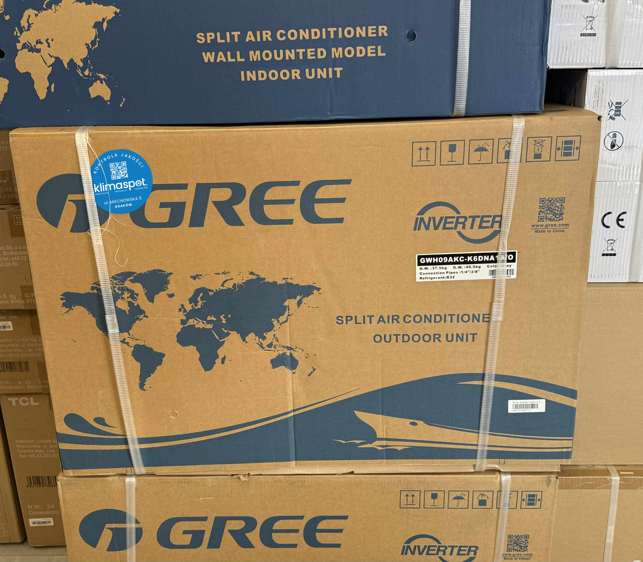 Kartonowe opakowania klimatyzacji Gree, model split, z oznaczeniami jednostki wewnętrznej i zewnętrznej, zabezpieczone taśmą. Widoczny znak kontroli jakości Klimaspot.