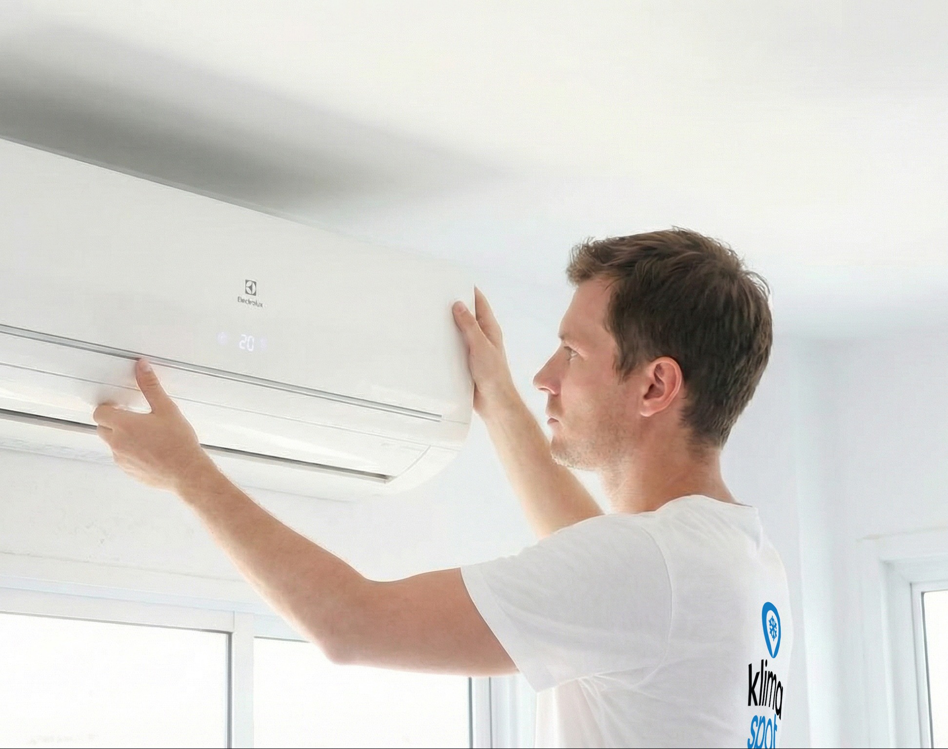 Mężczyzna instaluje białą klimatyzację Electrolux w jasnym pomieszczeniu. Widoczny wyświetlacz z temperaturą 20 stopni. Na koszulce logo firmy.
