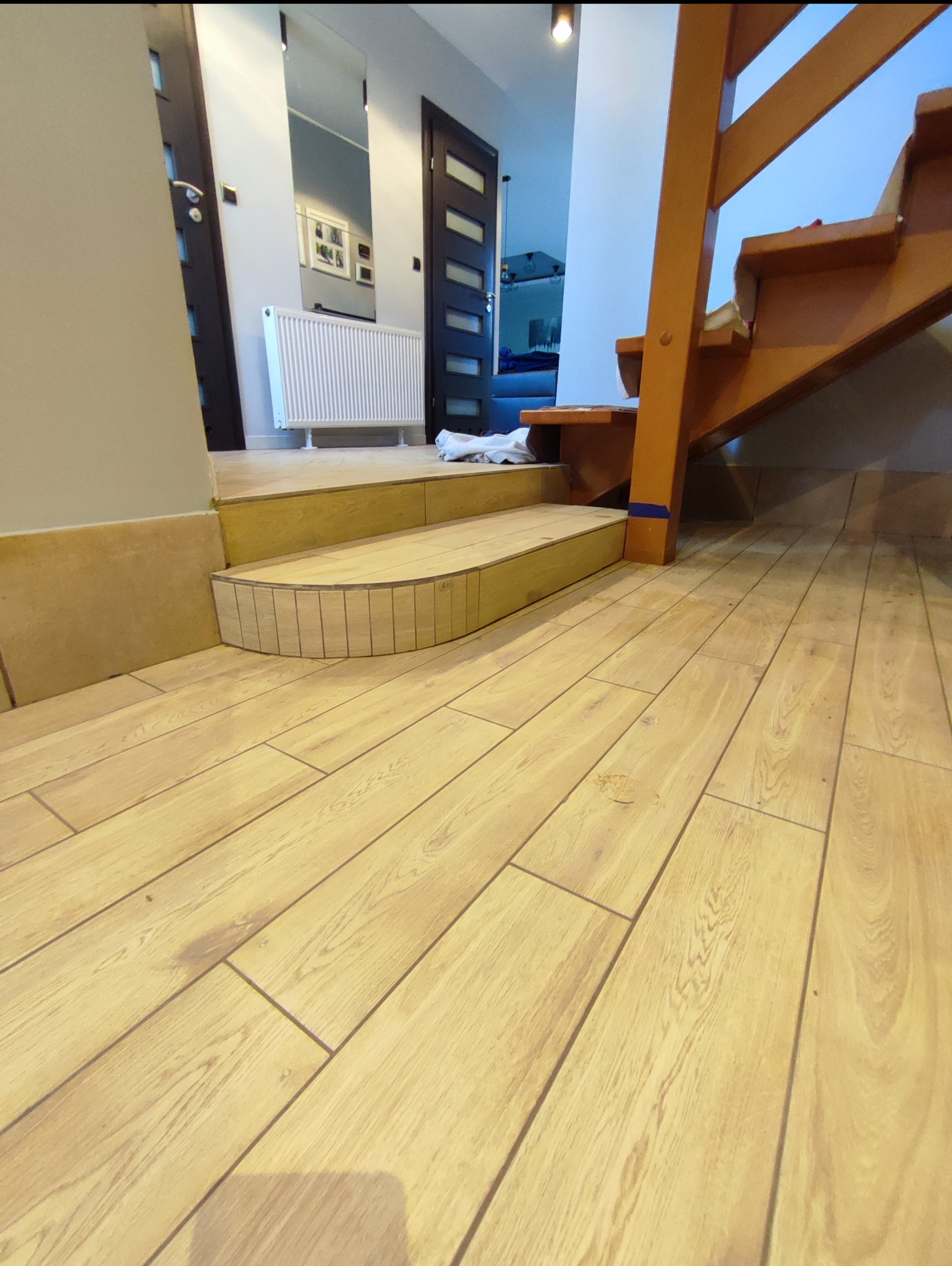 Ukończone schody z drewnianymi panelami podłogowymi, z zaokrąglonym wykończeniem stopnia. Widoczny fragment drewnianych schodów i grzejnik.