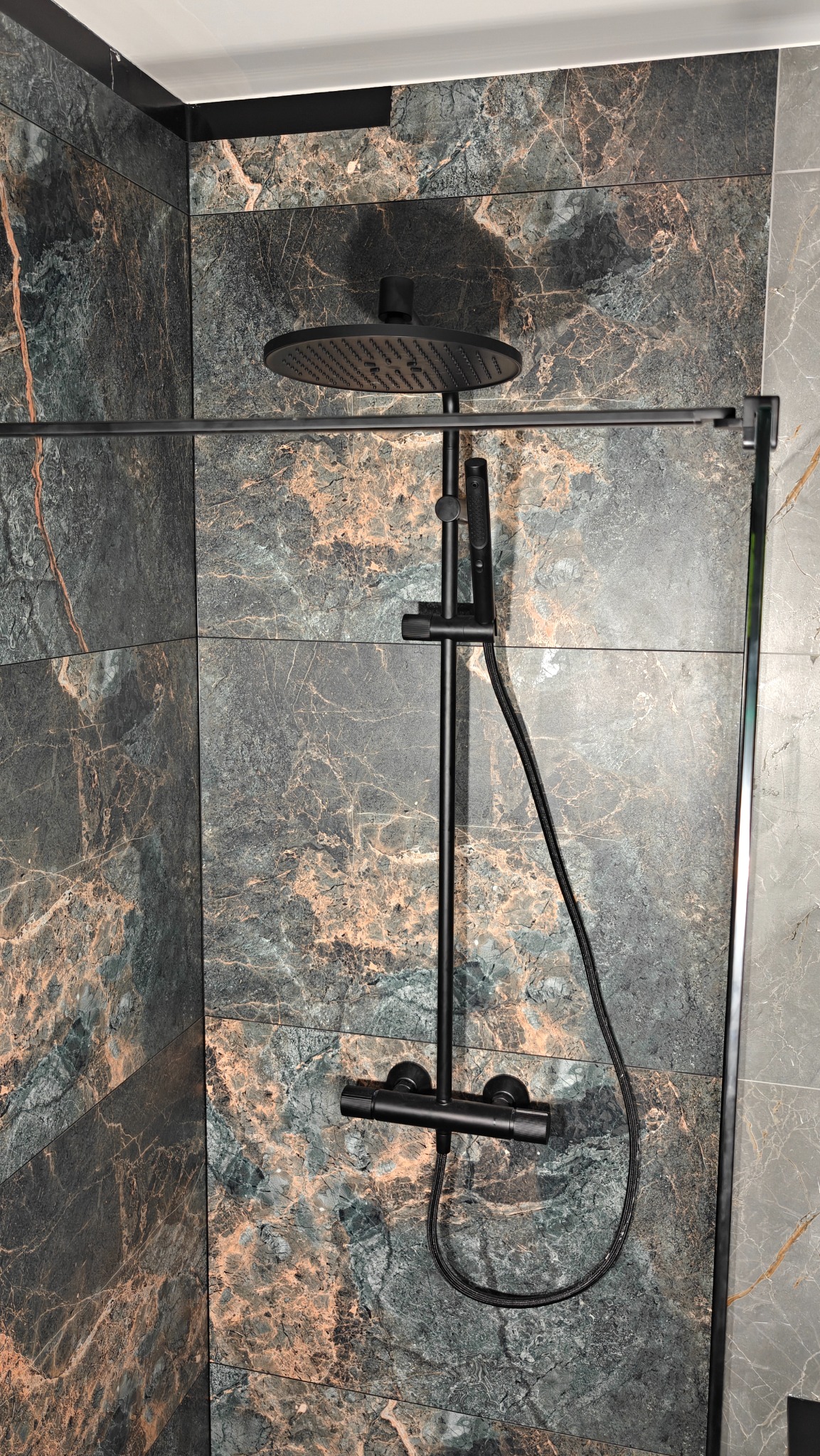 Nowoczesna kabina prysznicowa z deszczownicą i baterią w kolorze czarnym, na tle płytek imitujących marmur. Minimalistyczny design, eleganckie wykończenie.
