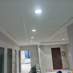 Andrzej Wiatr - Sufit podwieszany z płyt karton-gips z widocznymi punktami świetlnymi i elementami konstrukcyjnymi, w trakcie prac wykończeniowych. Widoczne narzędzia i sprzęt budowlany.