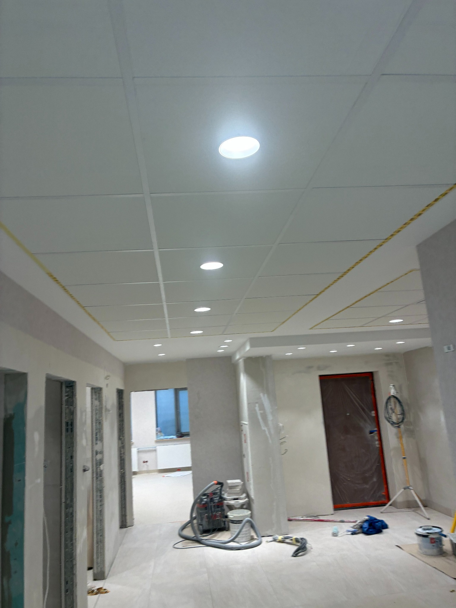 Sufit podwieszany z płyt karton-gips z widocznymi punktami świetlnymi i elementami konstrukcyjnymi, w trakcie prac wykończeniowych. Widoczne narzędzia i sprzęt budowlany.
