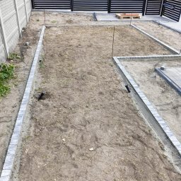 GREENGARDEN Łukasz Jaskólski - Przygotowanie terenu pod kostkę brukową: obrzeża ułożone, teren wyrównany, widoczne rury nawadniające. W tle nowoczesne ogrodzenie panelowe i dom.