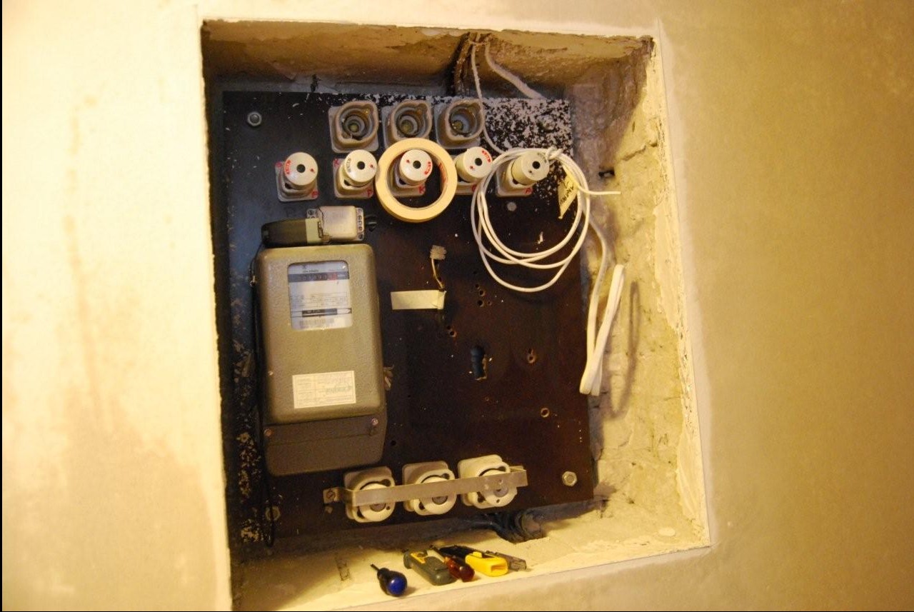 Tablica z bezpiecznikami i licznikiem energii elektrycznej wnęce ściany, widoczne narzędzia. Układ elementów wskazuje na etap prac podczas modernizacji instalacji.
