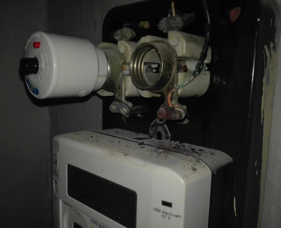 Stara skrzynka bezpiecznikowa z licznikiem energii elektrycznej, widoczne ślady korozji i zabrudzenia. Usługi elektryczne w Żukowie.