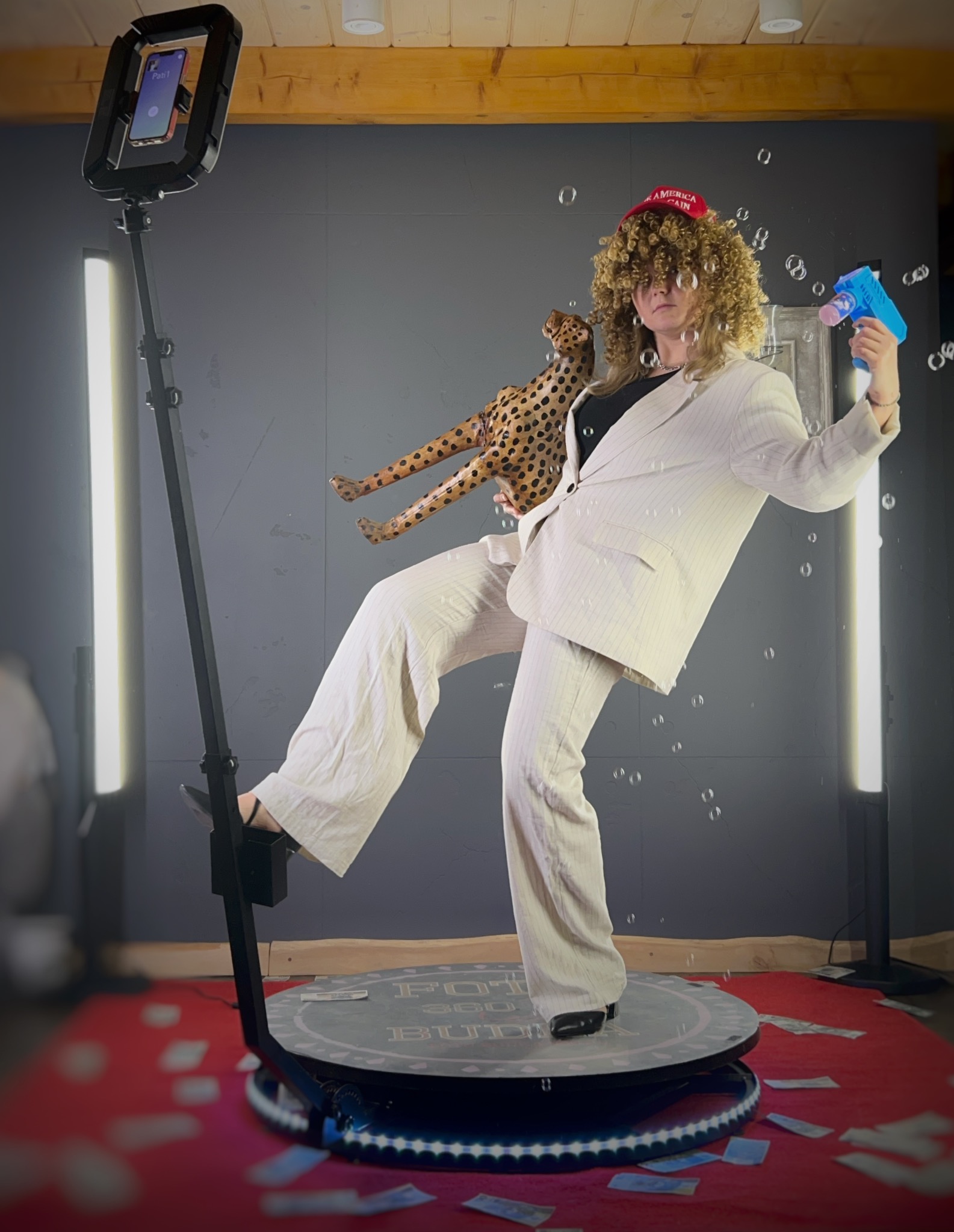 Osoba w garniturze pozuje z rekwizytami na platformie fotobudki 360, otoczona bańkami i sztucznymi pieniędzmi. Nietypowa stylizacja i dynamiczna scena.