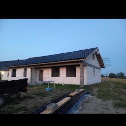 Mistrz-Bud - Niedokończony dom jednorodzinny z ciemną dachówką, widoczny z zewnątrz, w trakcie budowy. Ściany z białych pustaków, brak okien. Częściowo ułożona dachówka.