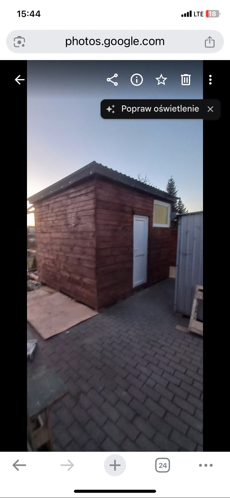 Drewniany domek narzędziowy z białymi drzwiami i oknem, świeżo po impregnacji, na tle kostki brukowej. Widoczne elementy konstrukcyjne i detale wykończeniowe.