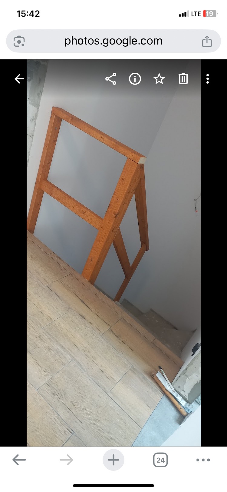 Drewniana konstrukcja schodów z bejcowanego drewna, widoczna na tle białej ściany i podłogi wyłożonej płytkami imitującymi drewno. W tle schody w stanie surowym.