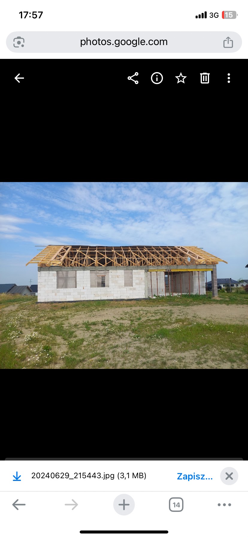 Budowa domu jednorodzinnego w stanie surowym otwartym: białe bloczki, drewniana konstrukcja dachu, widok z zewnątrz na tle błękitnego nieba i zieleni.