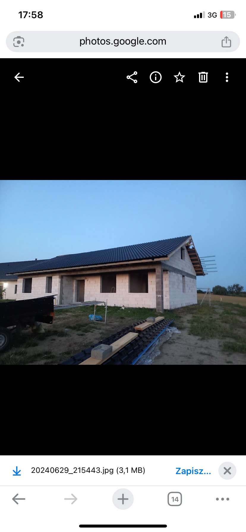 Niedokończony dom jednorodzinny z ciemną dachówką, widoczny z zewnątrz, w trakcie budowy. Ściany z białych pustaków, brak okien. Częściowo ułożona dachówka.