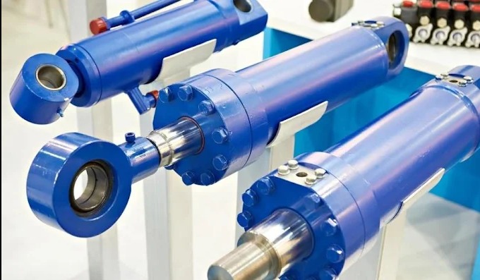 Niebieskie cylindry hydrauliczne z metalowymi elementami, ustawione w rzędzie, prezentowane na jasnym tle. Widoczne detale połączeń i konstrukcji.