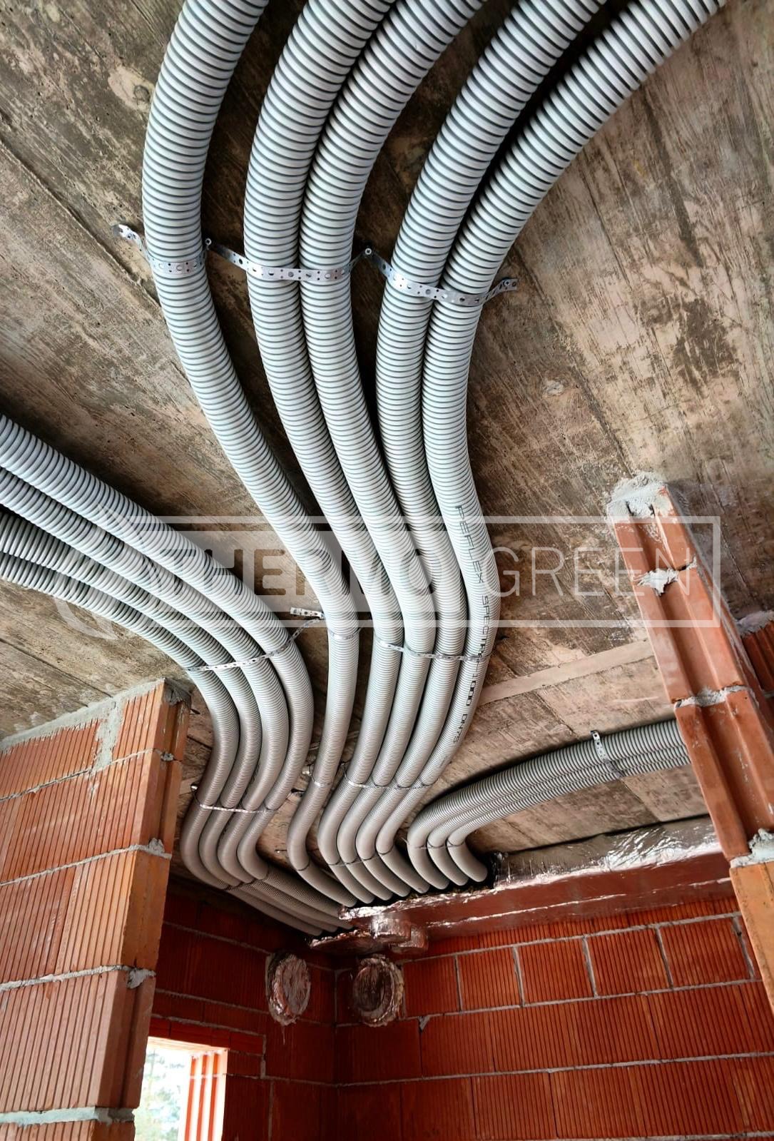 Szare, karbowane rury wentylacyjne przymocowane do sufitu w surowym stanie, widoczne ceglane ściany. Instalacja w trakcie budowy, z bliska.