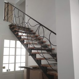 Alfa f.p.h.u - Nowoczesne schody metalowe z drewnianymi stopniami i ozdobną, kręconą balustradą, częściowo zabezpieczone folią, w jasnym wnętrzu domu.