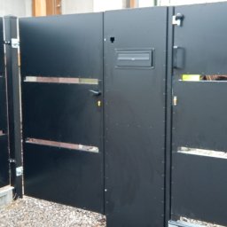 Alfa f.p.h.u - Nowoczesna, czarna brama wjazdowa z furtką i skrzynką na listy, z poziomymi prześwitami, zamontowana na posesji z szarą nawierzchnią żwirową.